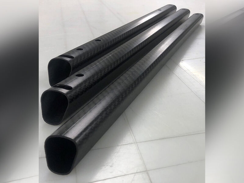 Images shows three non-cylindrical carbon fiber tubes of variable length laying side-by-side on a white surface. There are machined holes visible in the tubing. 